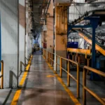 Interior pabrik manufaktur modern dengan mesin industri dan lini konveyor, menggambarkan proses produksi perusahaan manufaktur